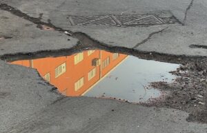 Urban street puddle reflecting orange building. Grungy city street scene with cracks and textures.