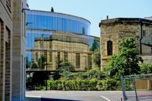 A modern glass building reflects an old stone building
